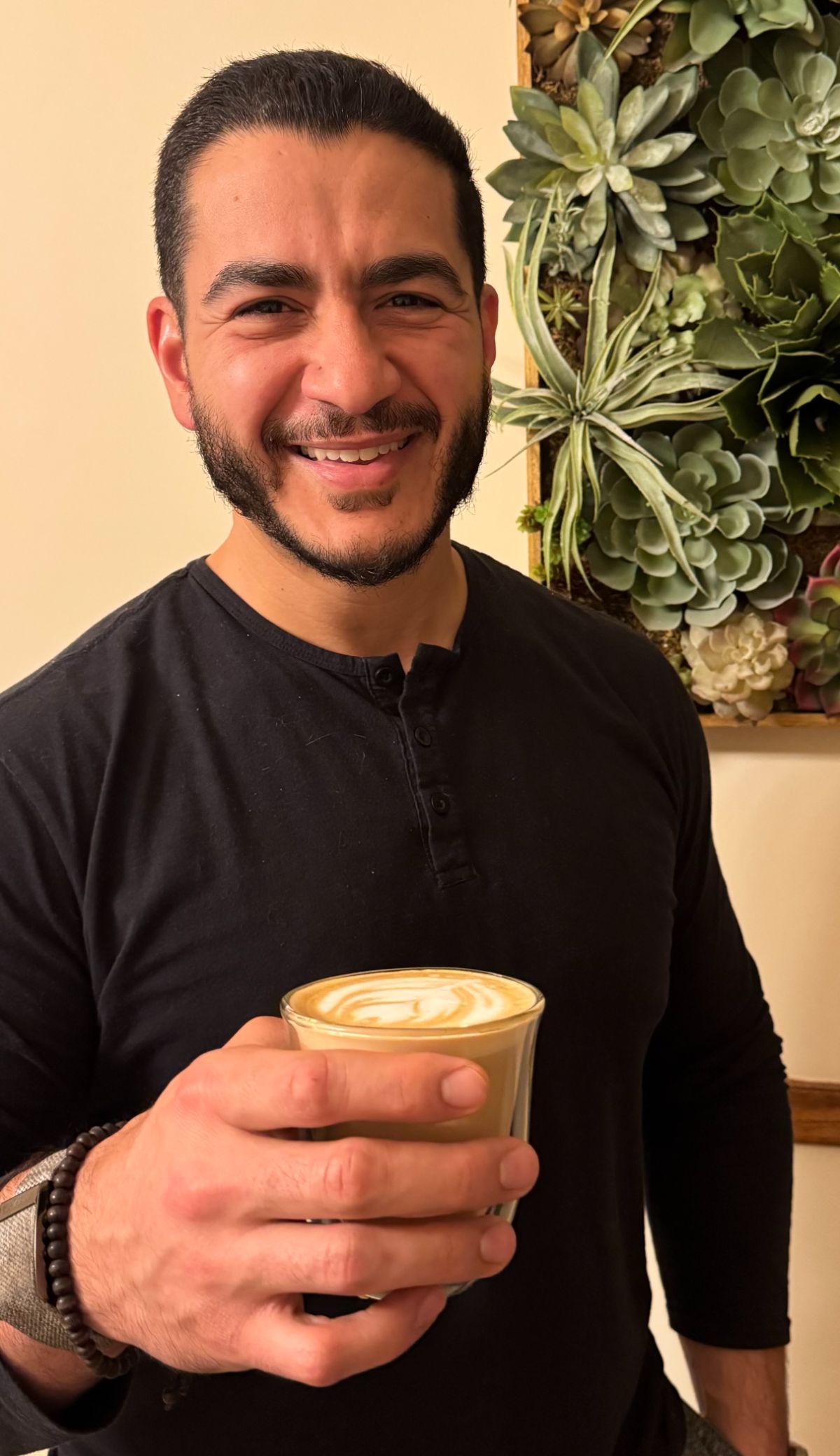 Abdul smiling while holding a cup of coffee